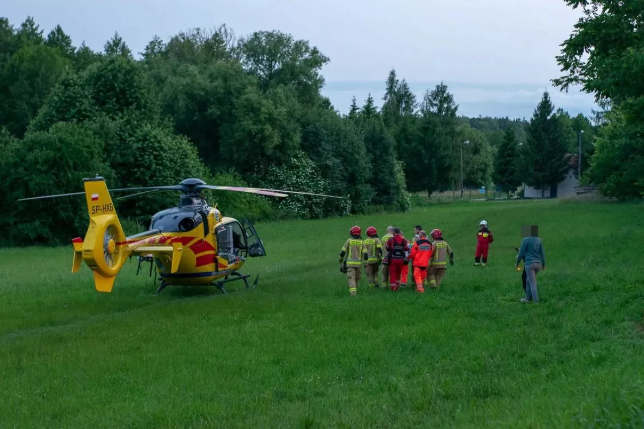Strażacy transportują rannego do helikoptera Lotniczego Pogotowia Ratunkowego.